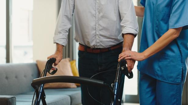 Nurse helping old man walk with a walker in a retirement home giving support. Closeup of a caregiver giving medical assistance to a disabled or handicapped mature man or patient